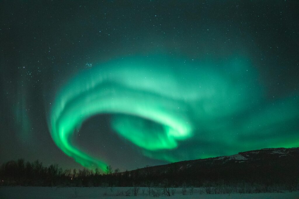 Northern Lights dancing over a mountain peak in Lapland, Finland – A breathtaking aurora display lighting up the Arctic sky above a snowy summit.