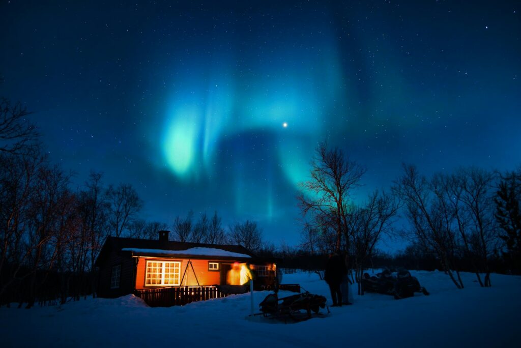Northern Lights above a rustic cabin in the Lapland wilderness – A magical aurora display lighting up the Arctic sky over a remote cabin.