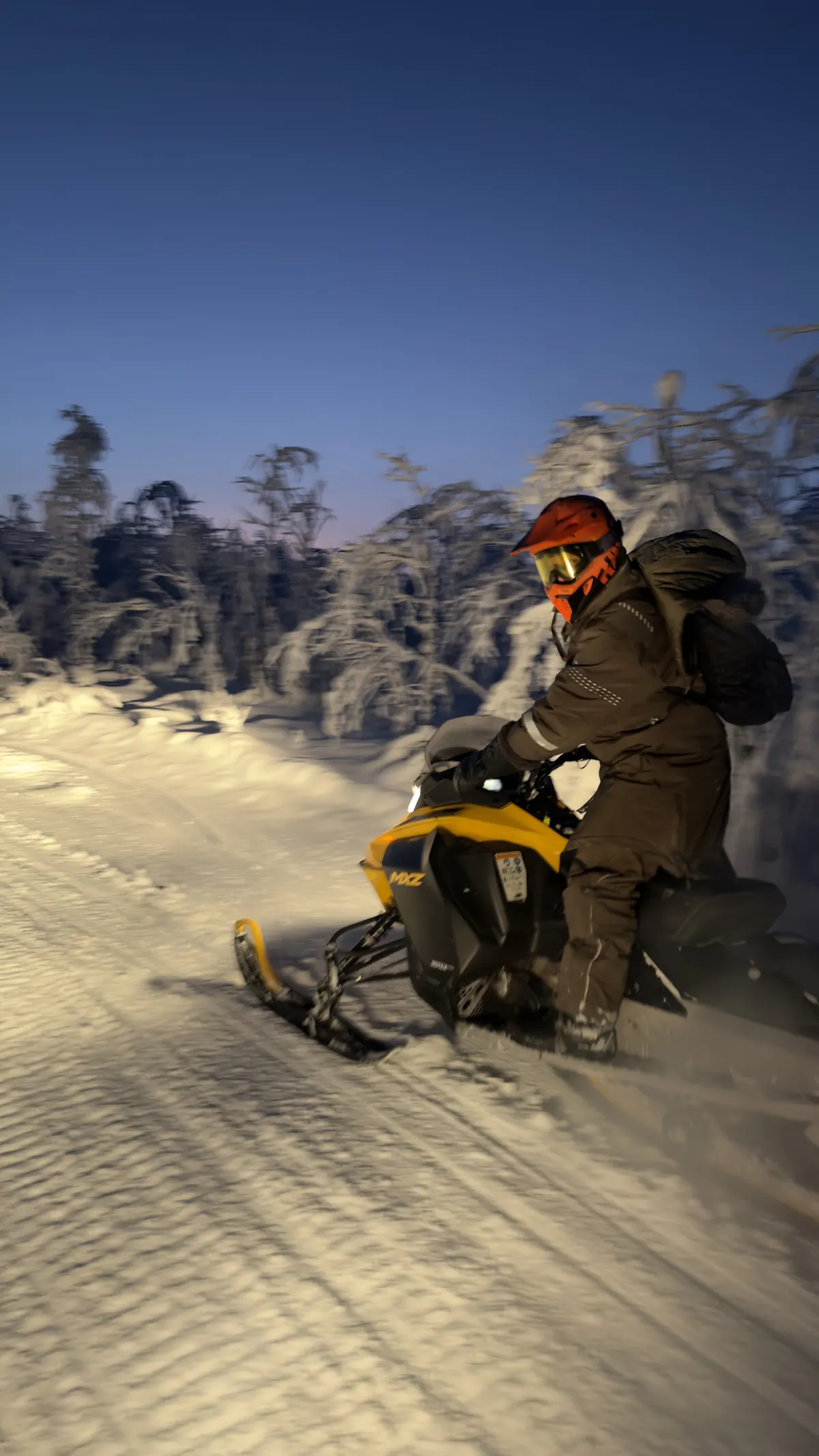 Moottorikelkkailija lumisessa metsässä iltahämärässä.