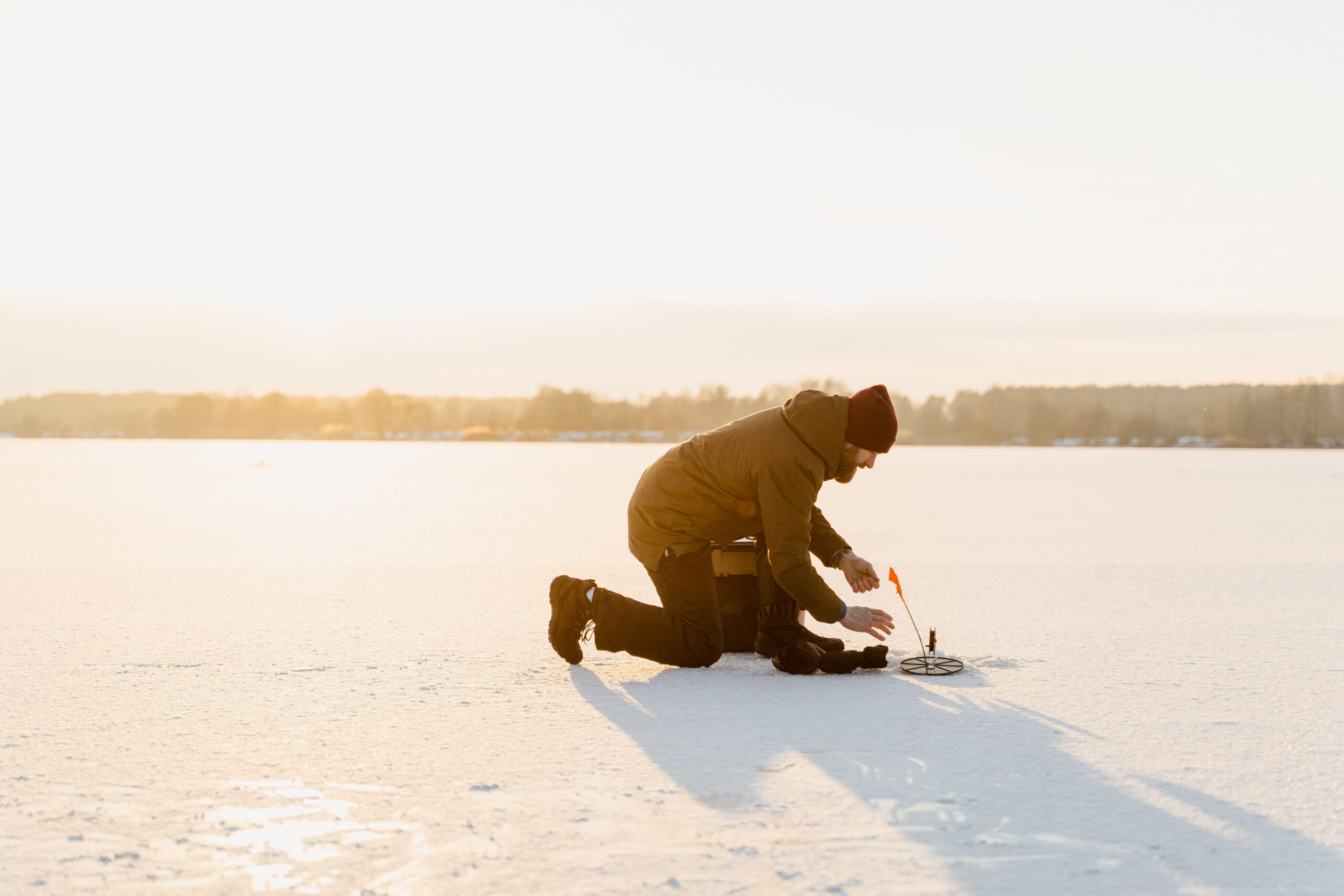 A person ice fishing on a snow-covered frozen lake in warm winter light