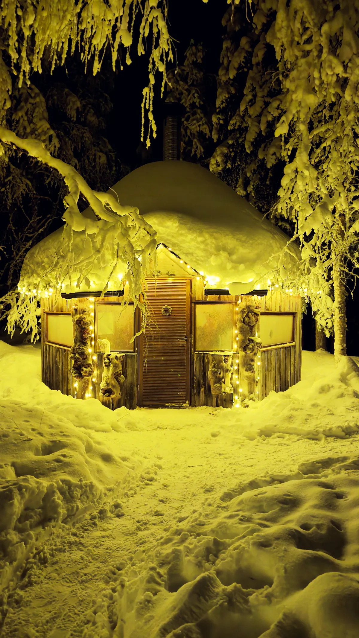 Lämmin valoketjuvalaistus lumisen kodan ympärillä talvisessa metsässä.